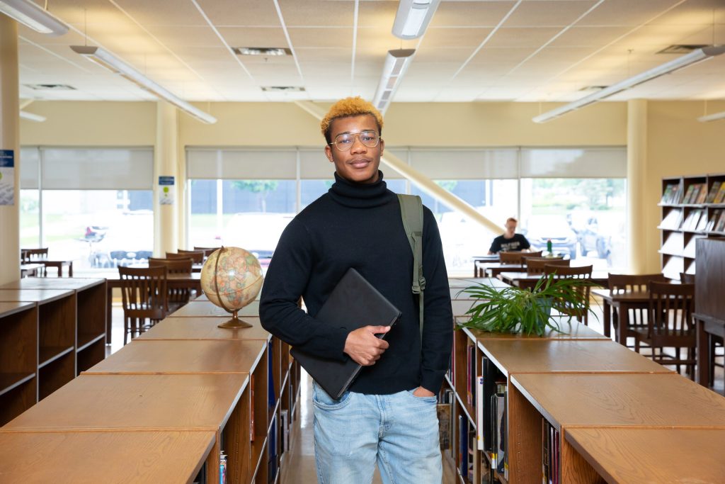 Un étudiant adolescent debout dans une bibliothèque avec un livre en main.