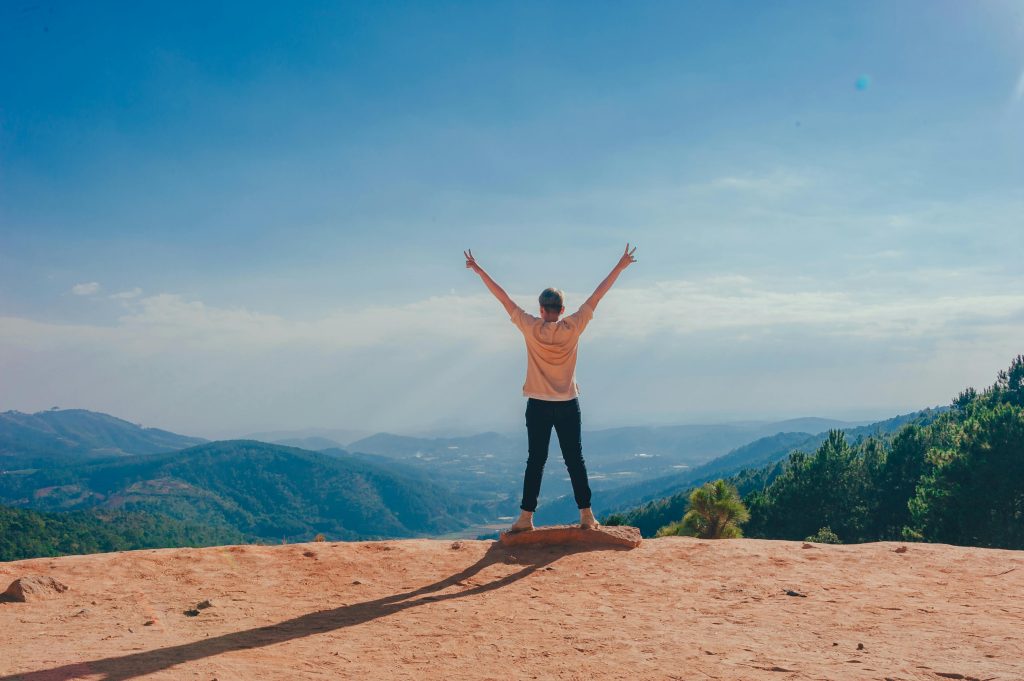 Enfant qui lève les bras au ciel devant un paysage montagneux