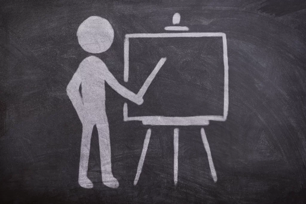 Dessin à la craie sur tableau noir représentant une silhouette pointant un tableau de présentation.