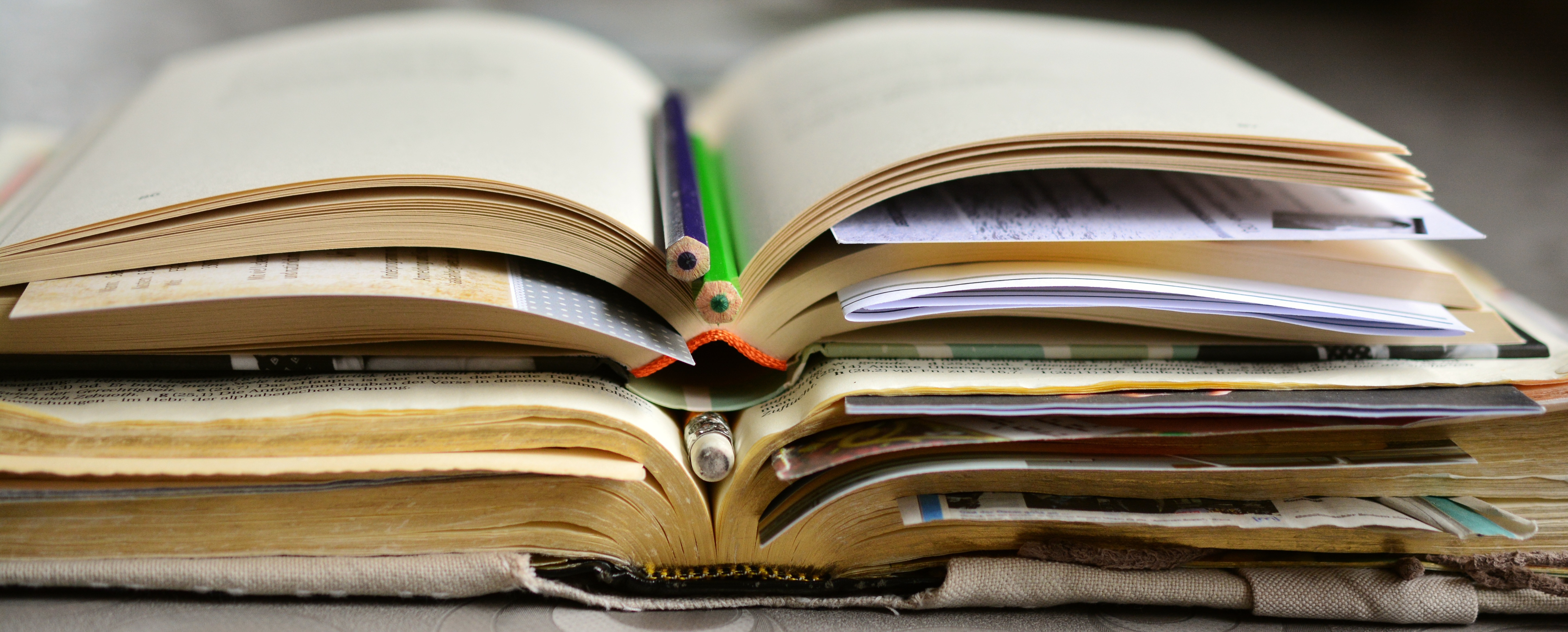 Gros plan sur une pile de livres ouverts avec des crayons, des feuilles et des marque-pages placés entre les pages.