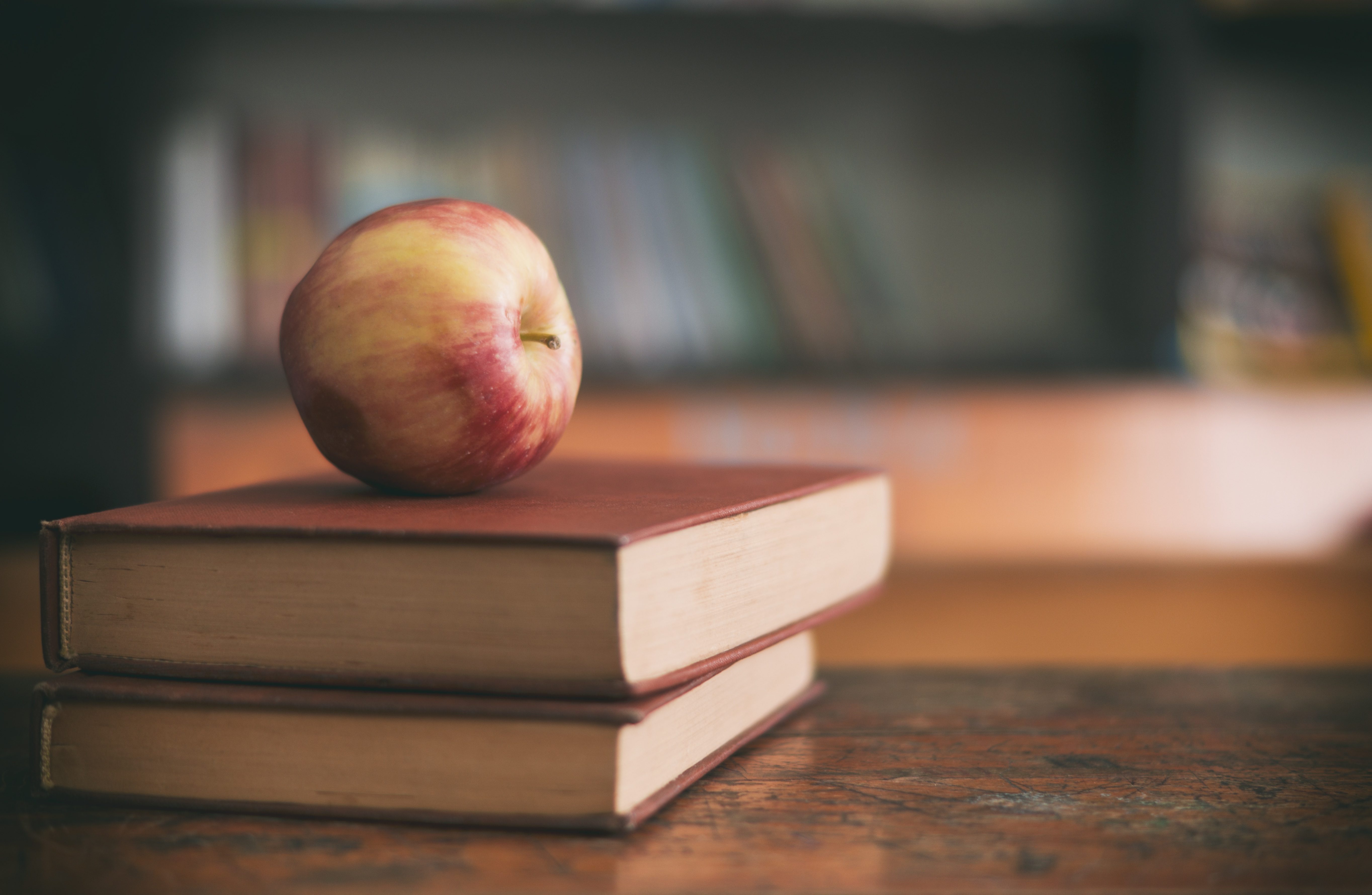 Une pile de deux livres sur un bureau, avec une pomme rouge sur la pile.
