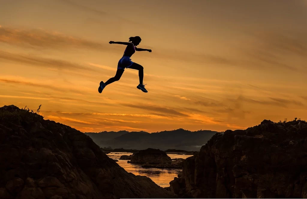Silhouette d'une femme sautant par-dessus un ravin entre deux rochers au coucher du soleil