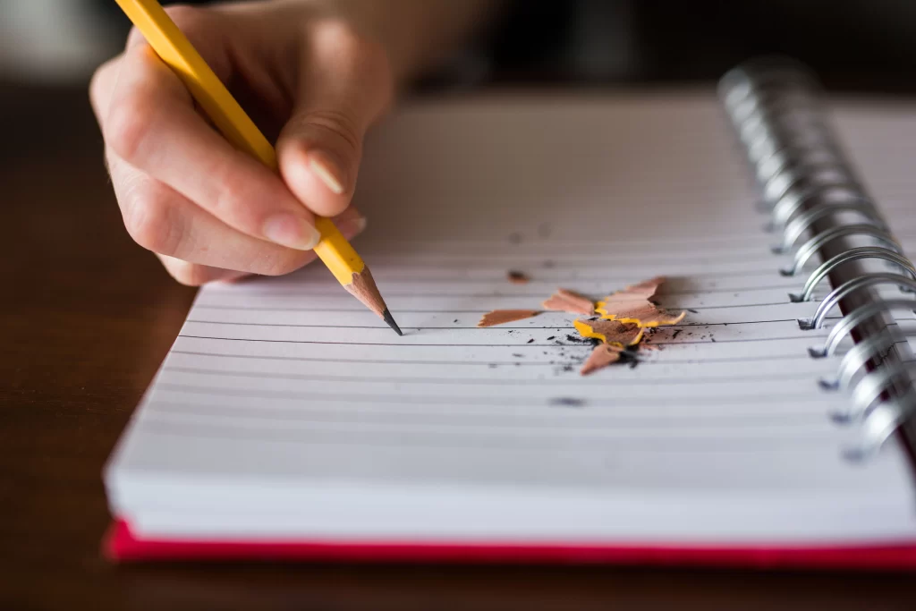 Gros plan d'une main tenant un crayon jaune et s'apprêtant à écrire sur un cahier à spirales ligné.